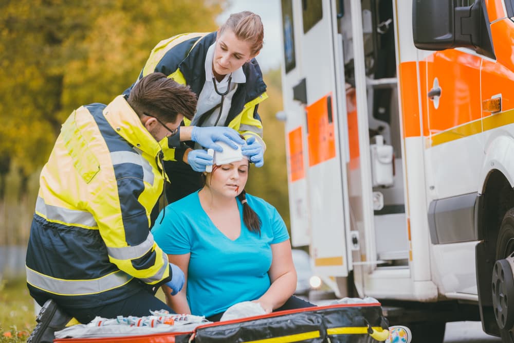 Medical responders attend to a woman's head injury with emergency dressing following an accident.